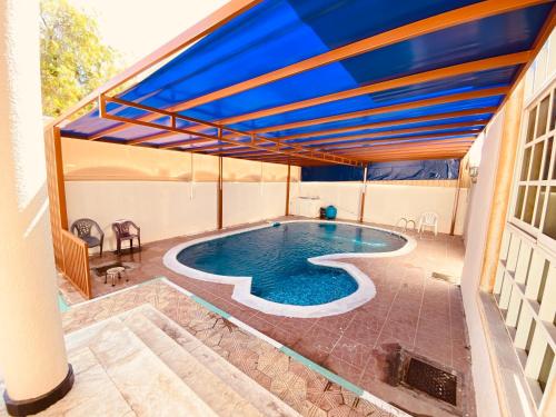 Holiday Home Rent villa في الشارقة: مسبح في بيت فيه مظلة زرقاء