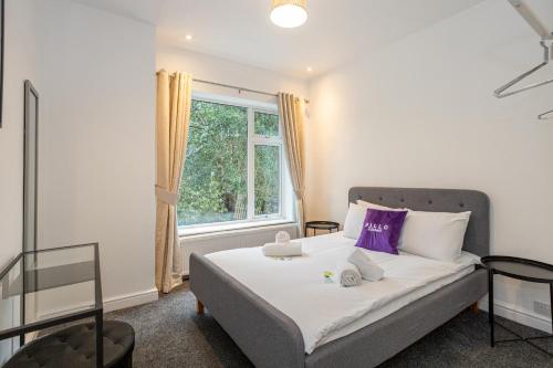 - une chambre avec un lit doté d'oreillers violets et d'une fenêtre dans l'établissement Pillo Rooms - Spacious 4 Bedroom Detached House close to Heaton Park, à Manchester