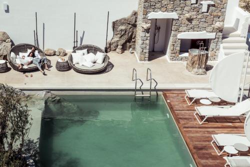 una piscina en una casa con gente sentada en sillas al lado en Kensho Ornos & Myconian Collection, en Ornos