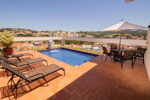 um pátio com uma piscina, cadeiras e um guarda-sol em Prado Hotel em Amparo