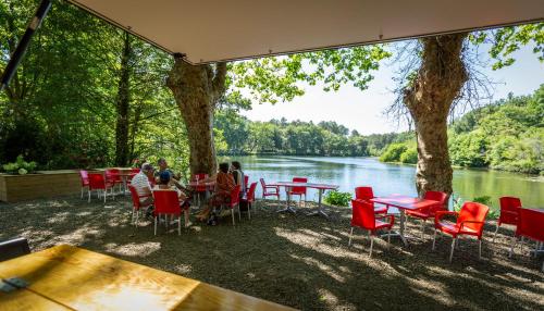 a group of people sitting at tables and chairs by a river at Camping L'Etang D'Ardy *** in Saint-Paul-lès-Dax