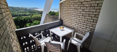 una mesa blanca y sillas en un balcón con vistas al océano en Pearly Shells, en Scottburgh