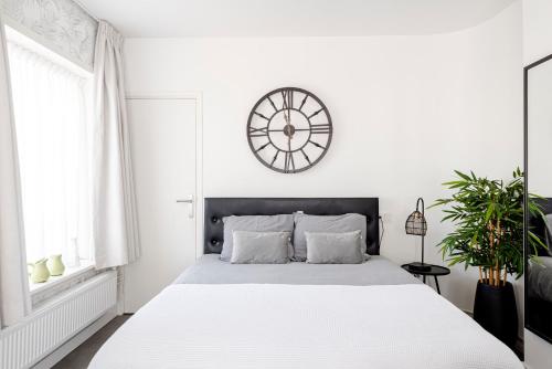 a white bedroom with a large bed and a clock on the wall at Beach&Dunes Studio in Zandvoort