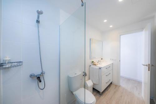 a white bathroom with a toilet and a glass shower at White suites in Cala d´Or