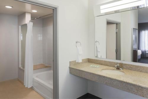 a bathroom with a sink and a mirror and a tub at Courtyard Austin Airport in Austin