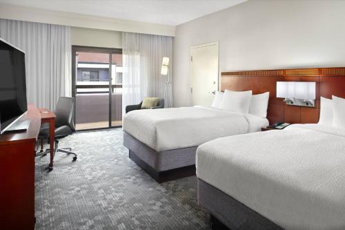 a hotel room with two beds and a desk and a television at Courtyard Greenville Haywood Mall in Greenville