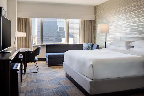 ダラスにあるシェラトン ダラス ホテルの白い大型ベッドとソファが備わるホテルルームです。