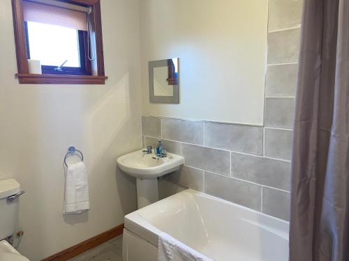 a bathroom with a sink and a bath tub and a toilet at The Wee Gem - 9 Milking Hill Park in Stornoway