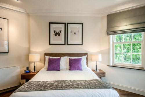 a bedroom with a bed with purple pillows and two windows at Chelsea - Sloane Avenue by Viridian Apartments in London