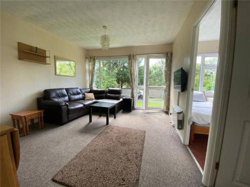 a living room with a black leather couch and a bed at 15 The Drive, Penstowe Holiday Park, Kilkhampton, Bude, Cornwall in Bude