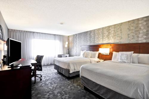 a hotel room with two beds and a flat screen tv at Courtyard by Marriott Jacksonville Airport/ Northeast in Jacksonville