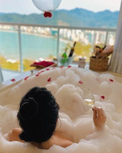 a woman laying in a foam bathtub with a wine glass at Hotel Pousada 7 Mares in Itapema