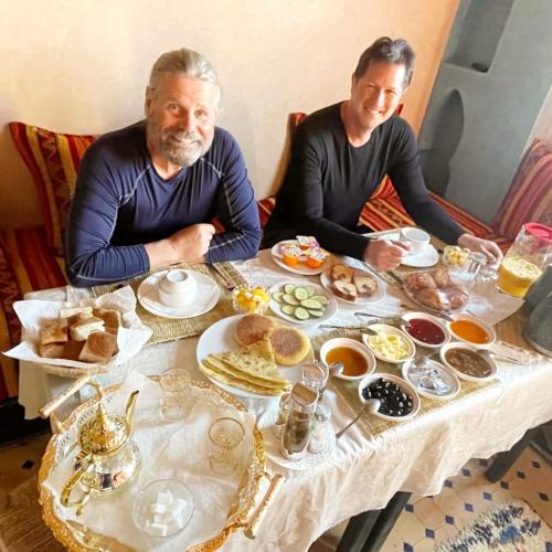 two men sitting at a table with food on it at Riad Hassi Labied Merzouga in Merzouga
