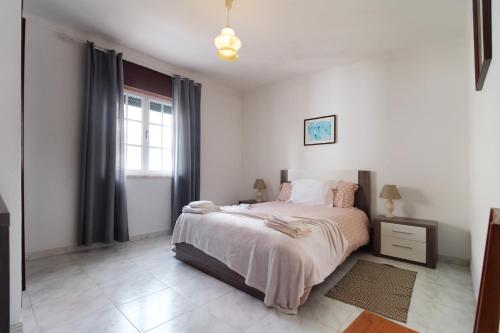 a white bedroom with a bed and a window at Casa da Avó in Vila Nova de Milfontes