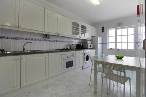 una cocina con armarios blancos y una mesa con sillas. en Casa da Avó, en Vila Nova de Milfontes