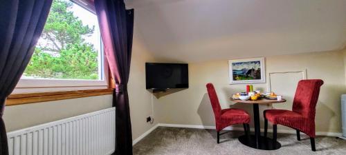 バルマカーラにあるSelf catering upper floor flat at Woodend houseのテーブル、赤い椅子2脚、窓が備わる客室です。