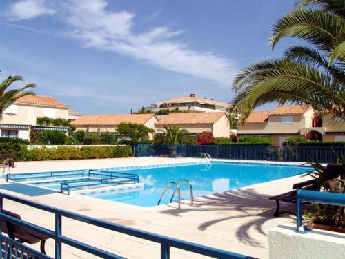 une grande piscine avec des palmiers et des maisons dans l'établissement Appartement familial avec piscine, terrasse et parking au Lavandou - 5 couchages - FR-1-251-487, au Lavandou
