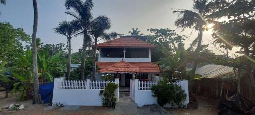 a house with a tower with a white fence and palm trees at Happy Seas Beach Villa in Alleppey