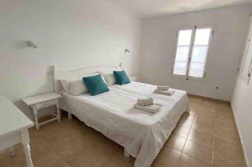 a white bedroom with a large bed with blue pillows at Calan Blanes con piscina in Ciutadella