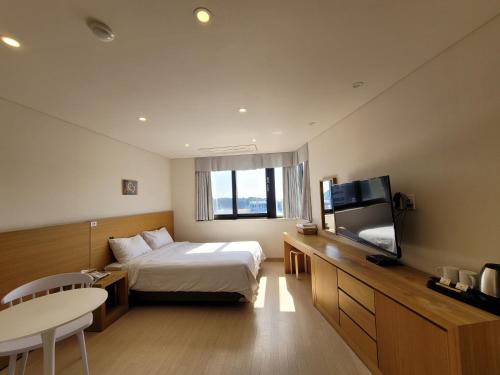 a hotel room with a bed and a tv and a table at BK Hotel Jeju in Seogwipo