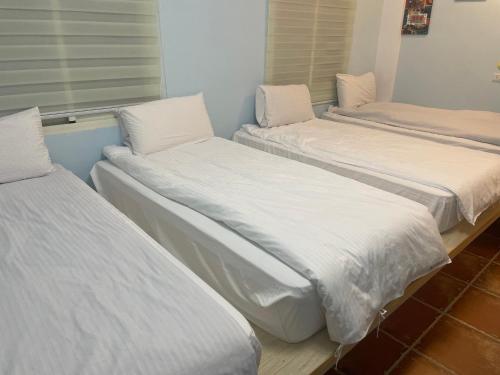 três camas num quarto com lençóis brancos em See Hualien Homestay em Hualien