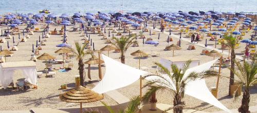 uma praia cheia de guarda-sóis e palmeiras em Hotel Sud Est by Fam Rossetti em Lavagna