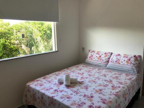 um quarto com uma cama com um cobertor florido e uma janela em Conforto e Aconchego em Imbassaí/BA em Imbassaí