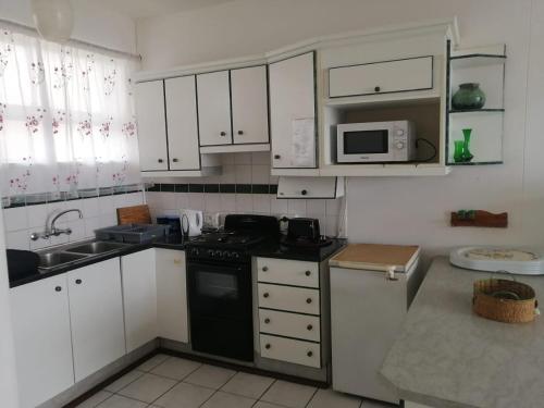 a kitchen with white cabinets and a black stove at Beach Road Holiday Apartment in Amanzimtoti