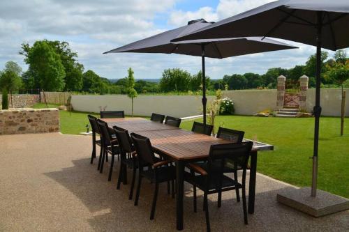 een houten tafel en stoelen met een parasol bij Gîte La Dortière s'Amuse, magnifique maison de maître 12min du Puy du Fo in Sevremont