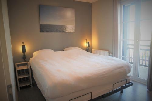 een slaapkamer met een groot wit bed en een raam bij Caramia, Duinhof, Romantic apartment by the sea in Cadzand-Bad
