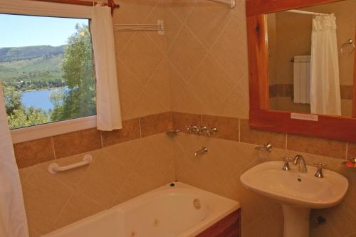 ein Bad mit einem Waschbecken, einer Badewanne und einem Fenster in der Unterkunft Hosteria Al Paraiso in Villa Pehuenia
