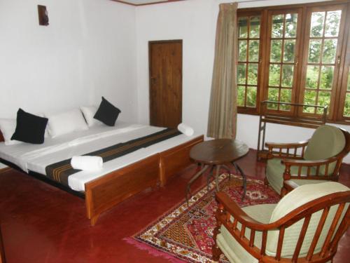 a bedroom with a bed and two chairs and windows at Hatale Mini World's End Bungalow in Madulkele