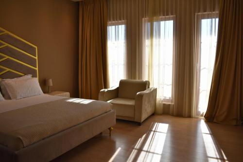 a bedroom with a bed and a chair and windows at Hotel Rezidenca Desaret in Berat