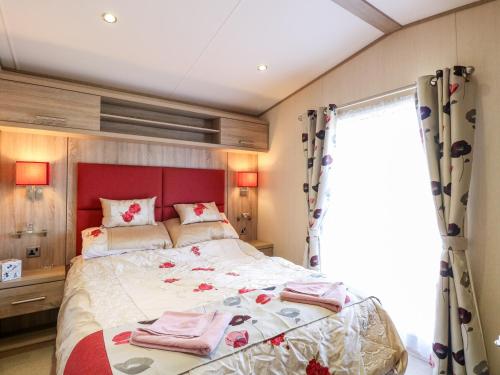 um quarto com uma cama com uma cabeceira vermelha e uma janela em Freddy's Lodge, Foxburrow Hang em Great Yarmouth