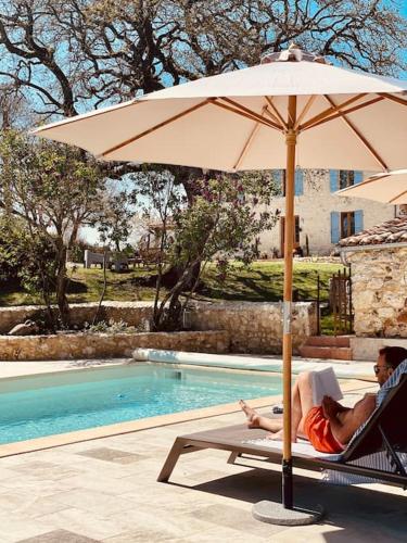 un homme assis sur une chaise sous un parasol à côté d'une piscine dans l'établissement Dôme insolite Lichen jacuzzi et petits-déjeuners inclus, à Gondrin