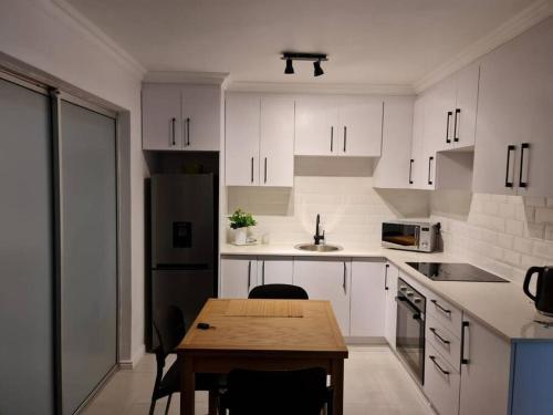 a kitchen with white cabinets and a wooden table at Cozy 2 bedroom APT - Near Kenilworth Racecourse in Cape Town