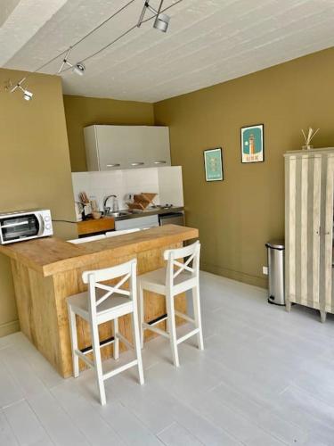 une cuisine avec deux tabourets blancs à un comptoir dans l'établissement Maison proche plages., à Benerville-sur-Mer
