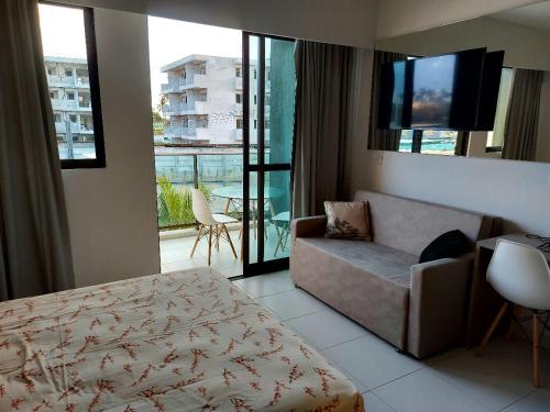 ein Hotelzimmer mit einem Bett, einer Couch und einem Fernseher in der Unterkunft Muro Alto Mana Beach Experience Apartamento B104 in Ipojuca