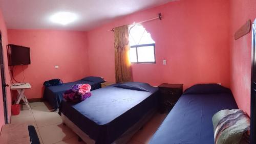 2 łóżka w pokoju z czerwonymi ścianami i oknem w obiekcie Hotel y Restaurante Tzutujil w mieście San Lucas Tolimán