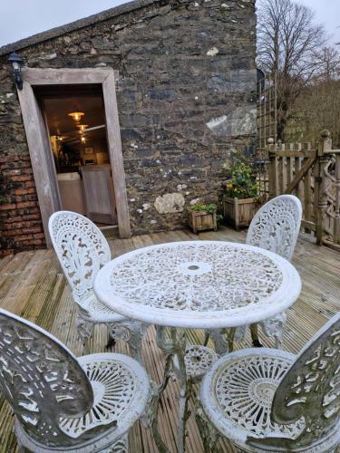 una mesa y sillas en una terraza con un edificio en Fyne Byre Cottage - Barn Conversion with Hot Tub en Cairndow