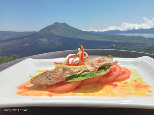 a plate of food with a piece of meat and tomatoes at Devanora Hotel & Resto in Kintamani