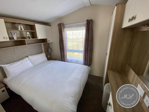 ein Schlafzimmer mit einem großen weißen Bett und einem Fenster in der Unterkunft Palm Grove 183 - Golden Palm - Pet friendly, WiFi, central heating, bed linen - Meadow Lakes Caravan & Lodge Hire in Chapel Saint Leonards