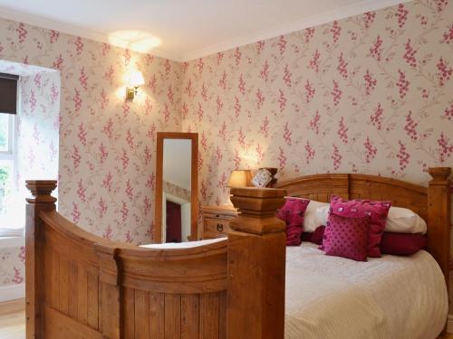 a bedroom with a wooden bed with pink floral wallpaper at Dairy Cottage - Beaufort Estate in Belladrum