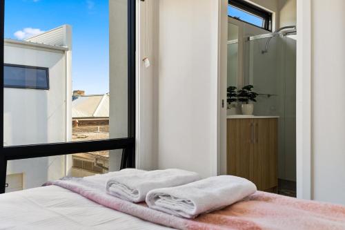 - une chambre avec des serviettes blanches sur un lit et une fenêtre dans l'établissement Swainson on College, à Port Adelaide