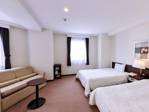 長野市にあるホテルコートランドのベッド2台とソファが備わるホテルルームです。