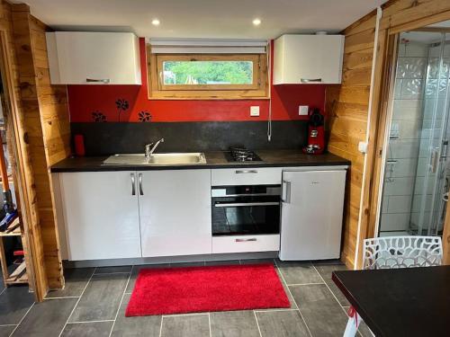 una cocina con armarios blancos, fregadero y alfombra roja en Chalet 2 personnes avec jacuzzi et piscine saisonnière en Corcieux