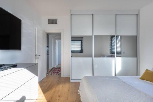 a white bedroom with a bed and a television at Boho Vibe in Tel Aviv