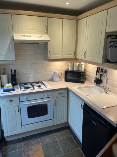 a kitchen with white cabinets and a stove and a sink at Wicket Green Cottage in Hayfield