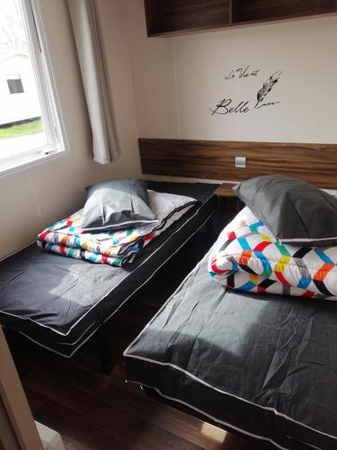 two beds sitting in a room with a window at MHVACANCES LOUENT PLUSIEURS MOBILHOMES DANS CAMPING 4 ETOILES PROCHE CHATEAUX et ZOO BEAUVAL in Onzain