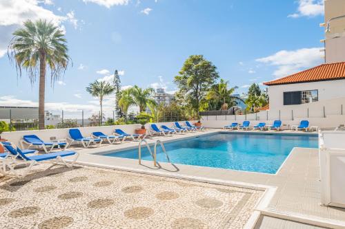 une piscine avec des chaises longues bleues et un bâtiment dans l'établissement Apartamento Casa Branca 360, à Funchal
